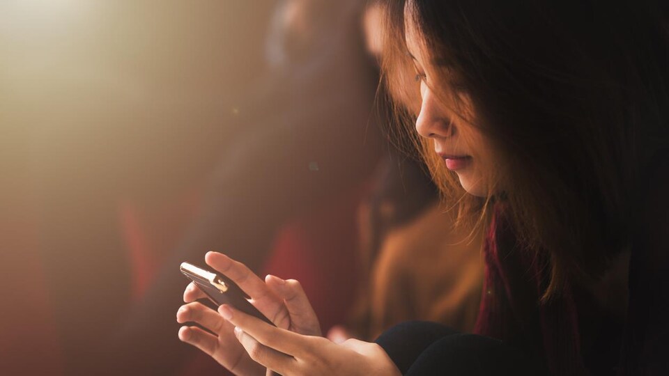 Gros plan sur une jeune femme asiatique, téléphone en main.