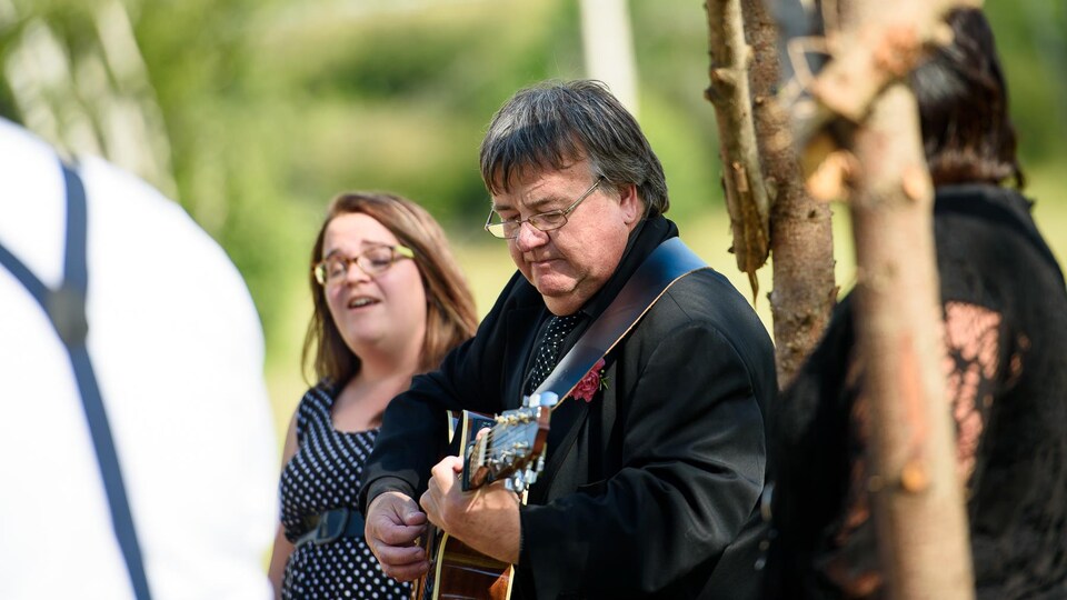 Paul Gallant accompagne à la guitare sa fille Adrienne, qui chante à un mariage en plein air.