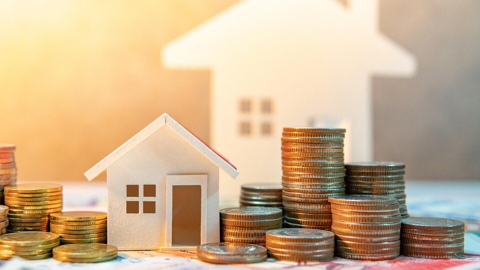 Un modèle d'une petite maison entourée de pièce de monnaie devant un modèle d'une plus grande maison.