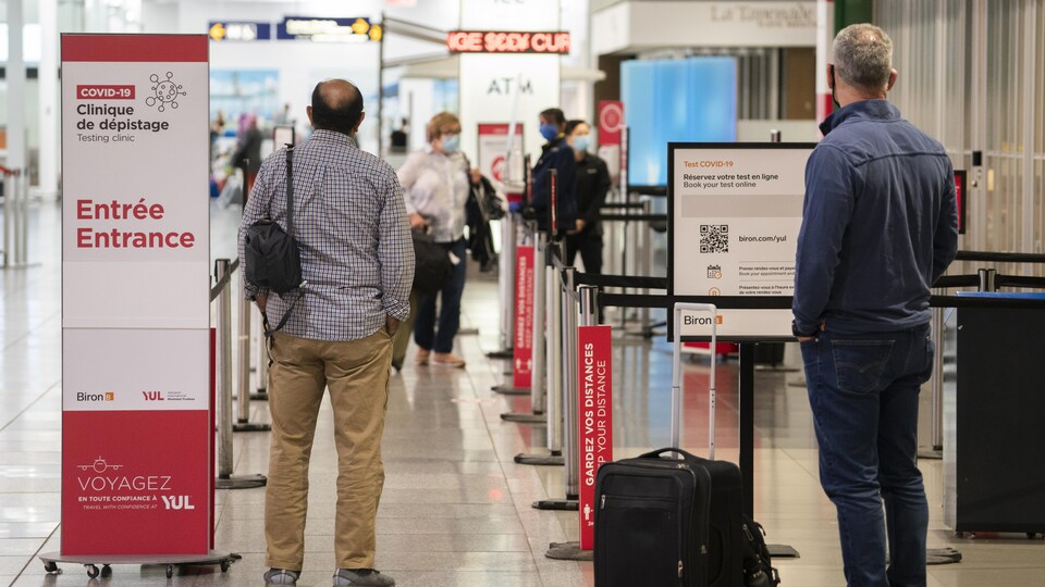 Des voyageurs attendent près d'un centre de dépistage à l'aéroport international Pierre-Elliott-Trudeau de Montréal.