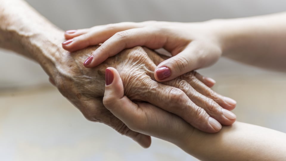 Une femme plus jeune tient la main d'une femme âgée.