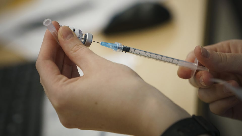 Manipulation d'une seringue et du vaccin contre la COVID-19.
