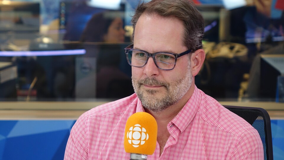 Un homme portant des lunettes derrière un micro dans un studio radio de Radio-Canada