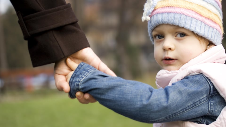 La main d'un parent tient celle d'un jeune enfant qui regarde par-dessus son épaule. 