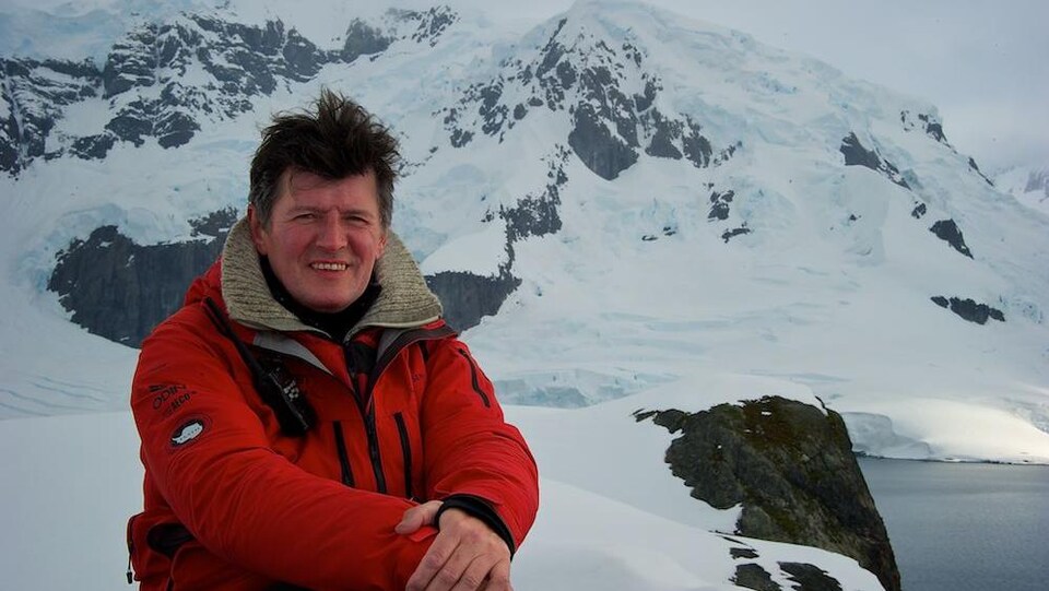 Un homme habillé chaudement assis en haut d'une montage couverte de neige.
