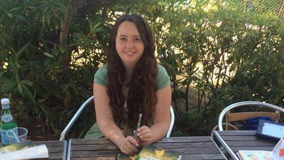 Amelia Jones assise à une table avec ses romans devant elle.