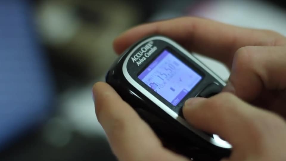 Deux mains tenant un appareil servant à mesurer le taux de glucose dans le sang. 