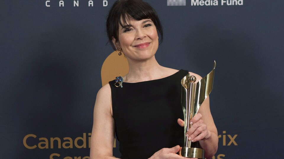 La comédienne pose pour les photographes en tenant le trophée de ces deux mains. Elle sourit.