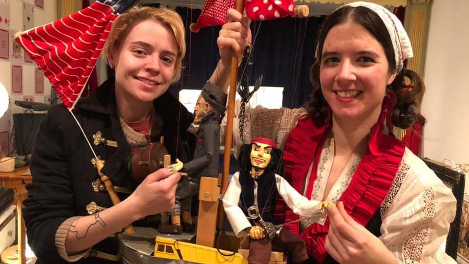 Anne-Marionnette vêtue d'un costume à dentelle montre sa marionnette du pirate Jack Sparrow sur son bâteau miniature à mât. 