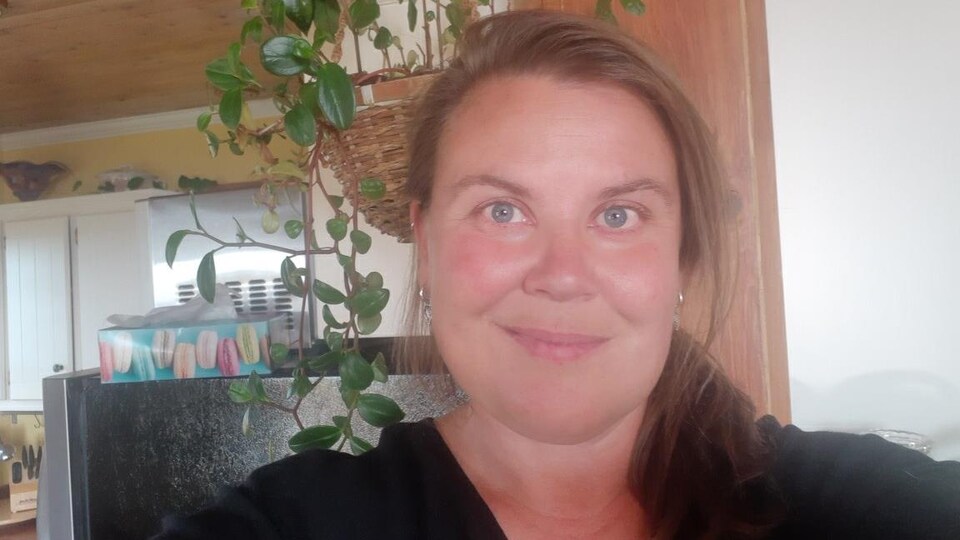 Une femme aux yeux bleus et cheveux longs châtains sourit à la caméra..