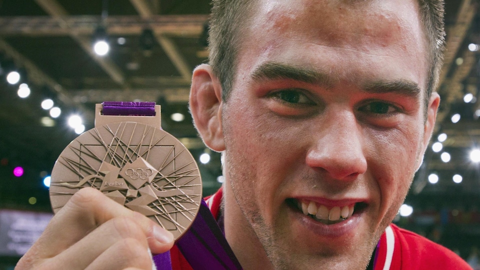 Antoine Valois-Fortier qui tient sa médaille de bronze près de son visage.