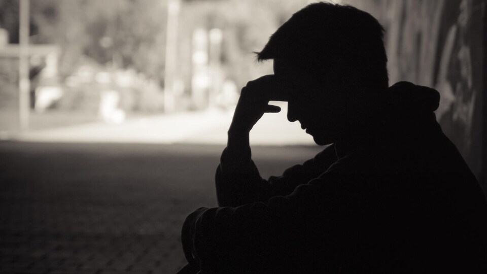 Un homme assis dans une rue sombre se tient le front.