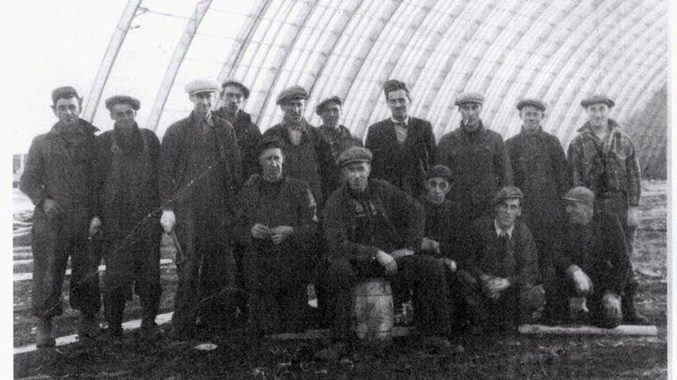 Photo d'archive noir et blanc , où on voit une quinzaine de travailleurs en 1954 sur le chantier de l'aréna Wendell-Chiasson à Cap-aux-Meules.