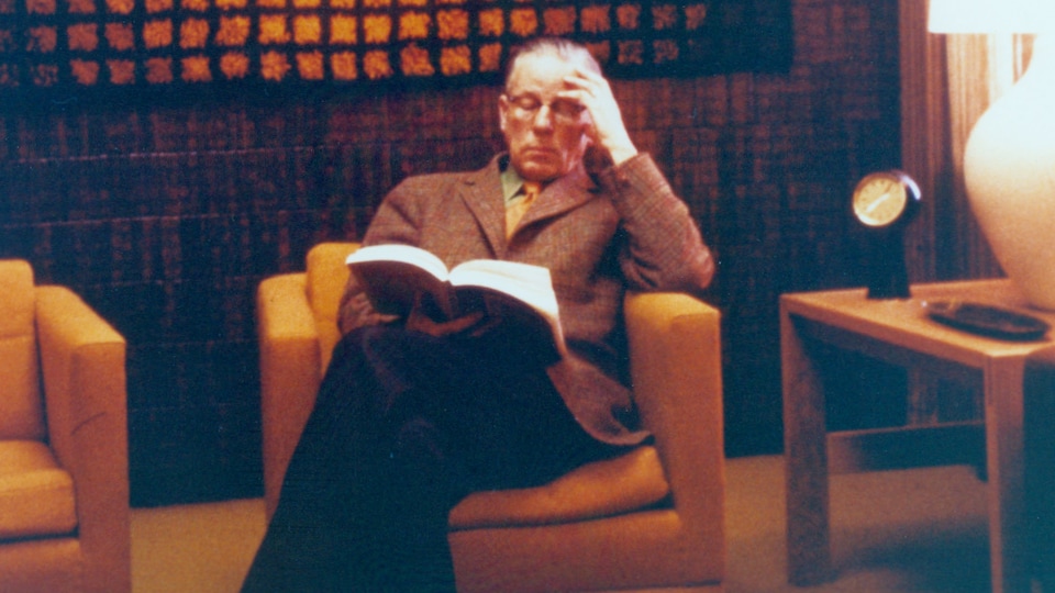 Armand Frappier lit un livre sur une chaise