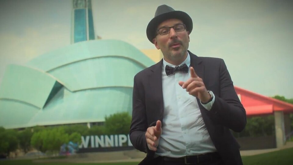 Un homme porte des lunettes et un chapeau, et il pointe son doigt