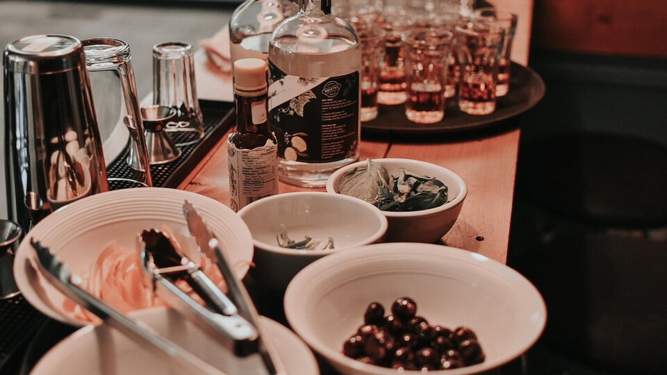 Des outils pour réaliser des cocktails, avec une bouteille d'alcool et des ingrédients frais.