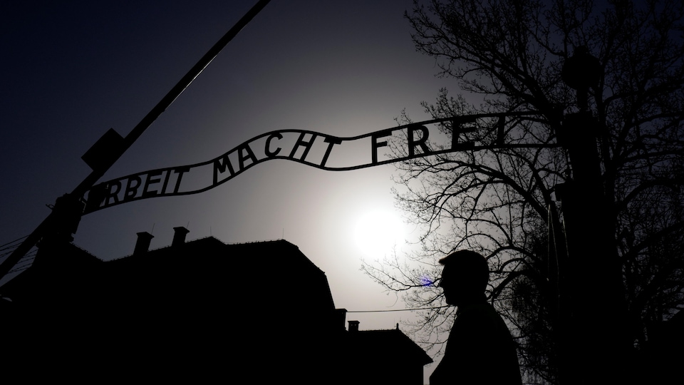 La photo prise à contre-jour  d'un portail en fer forgé arborant un slogan nazi, avec la silhouette d'une personne passant devant. 