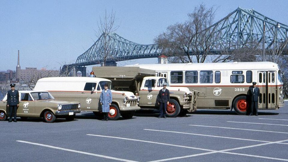 Photo d'époque de quatre véhicules bruns de la Société de transport de Montréal avec un homme debout devant chaque véhicule.