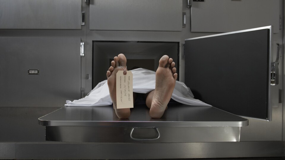 Un corps nu et mort recouvert d'un drap blanc dans un réfrigérateur dans une salle d'autopsie. 