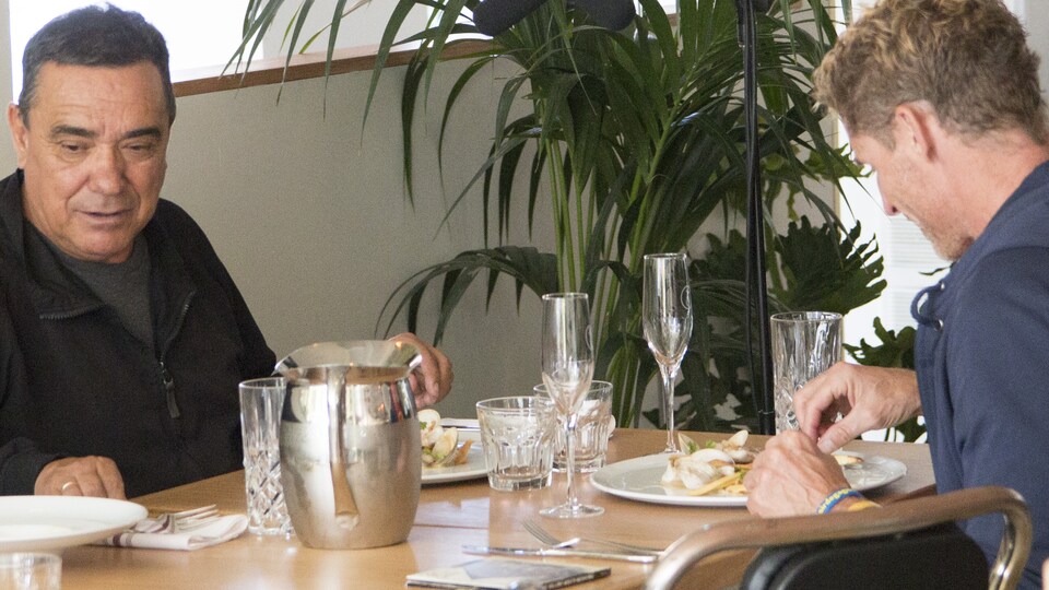 Les deux hommes sont assis à une table de restaurant.