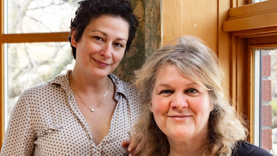 Les deux femmes sourient en posant près d'une fenêtre.