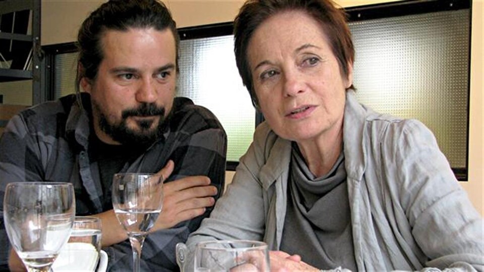 Les deux comédiens regardent au loin en étant assis à une table.