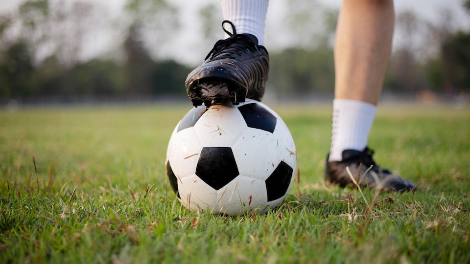 Gros plan sur le pied d'un joueur sur un ballon de soccer sur un terrain gazonné. 