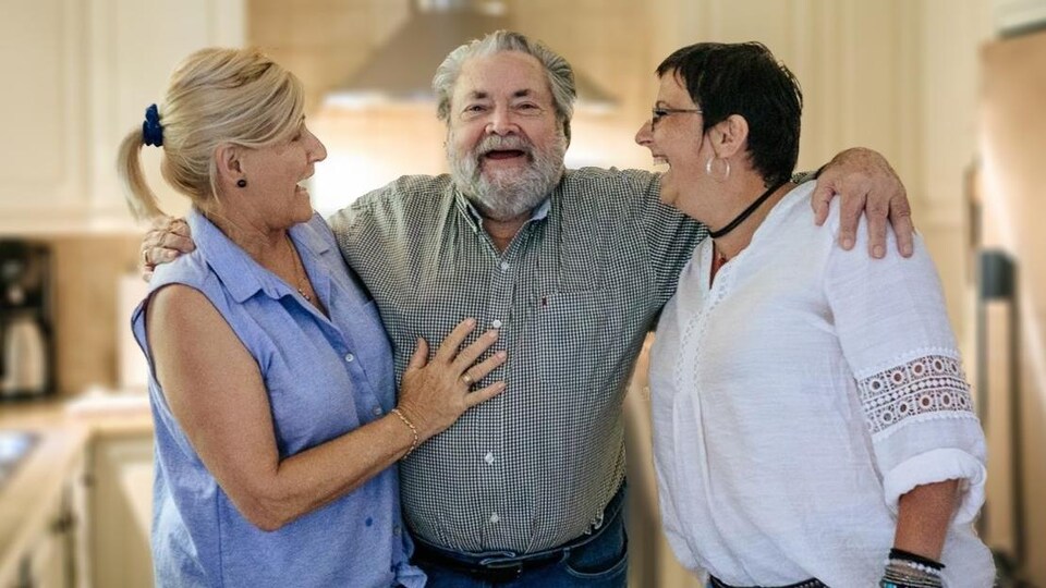 Un homme entourée de deux femmes souriants.