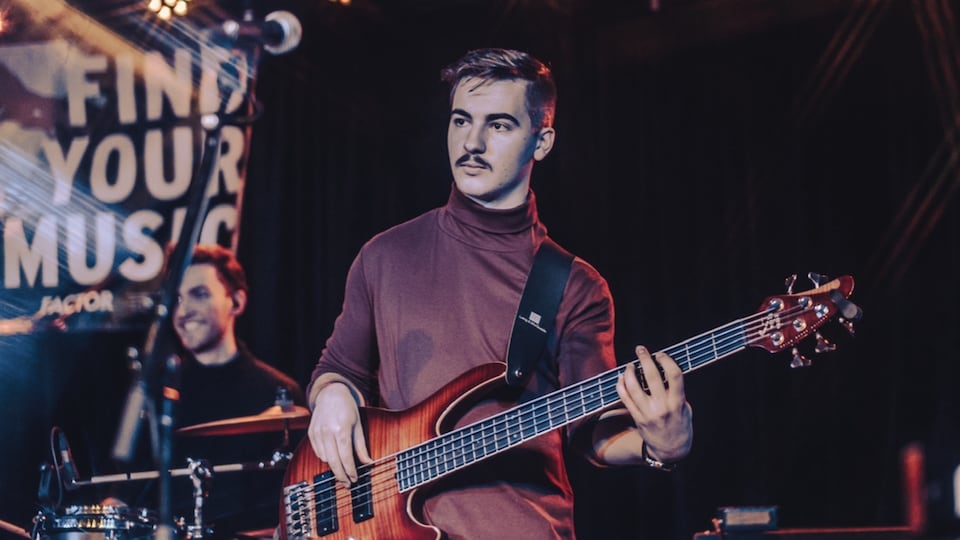 Marco Freynet, musicien, est présent sur une scène musicale jouant de la basse et se tenant devant un batteur.