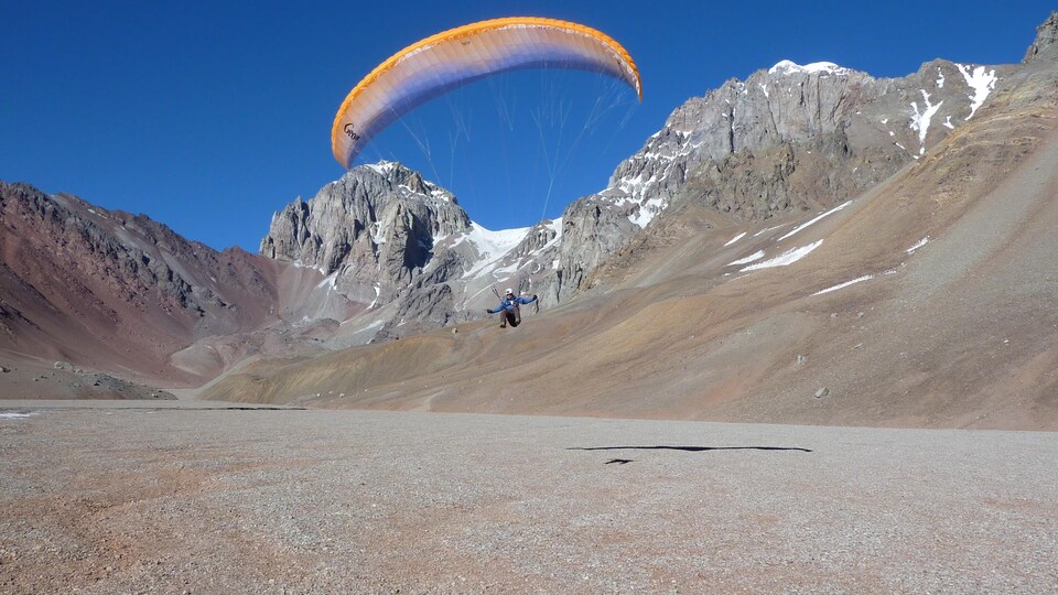 Un homme fait du parapente dans les montagnes avec du ciel bleu en arrière plan.