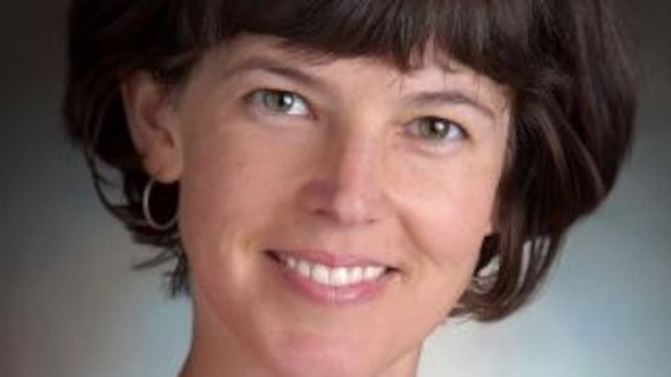 Une femme avec des cheveux bruns, elle sourit.