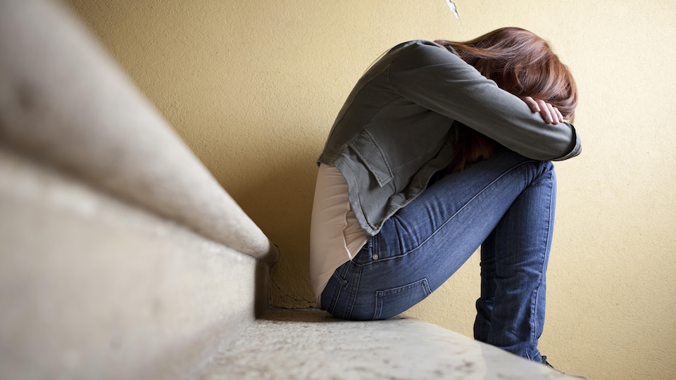 Une adolescente assise dans un escalier, elle a la tête dans ses bras. 