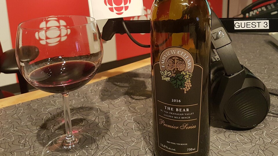 Une bouteille de vin rouge intitulé The Bear du domaine Fairview Cellars dans l'Okanagan à cöté d'un verre de vin