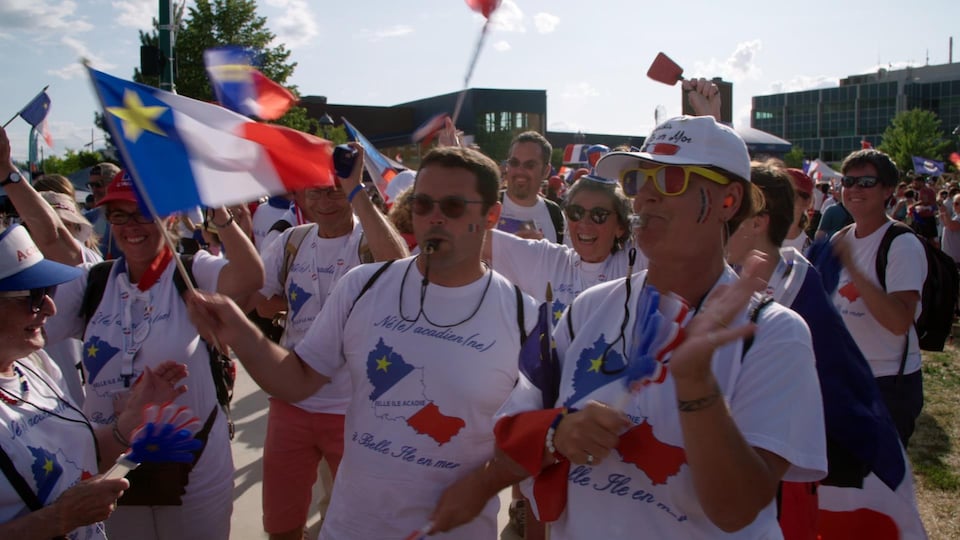 Des Bellilois, sifflets à la bouche, portant des chandails de l'Acadie et arborant des drapeaux de l'Acadie.