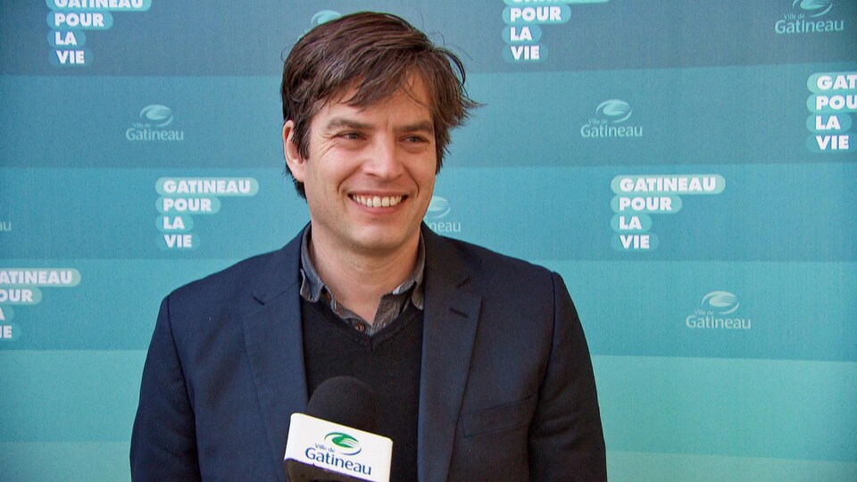 Benoit Dellage en entrevue devant un fond bleu portant l'inscription : Gatineau pour la vie. 