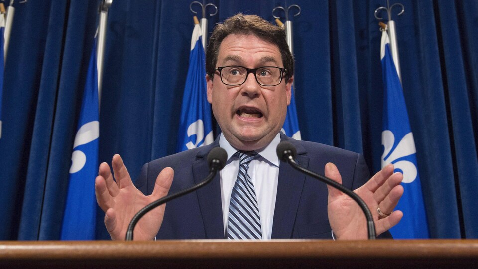 Bernard Drainville parle en agitant les mains derrière un lutrin lors d'une conférence de presse à l'Assemblée nationale.