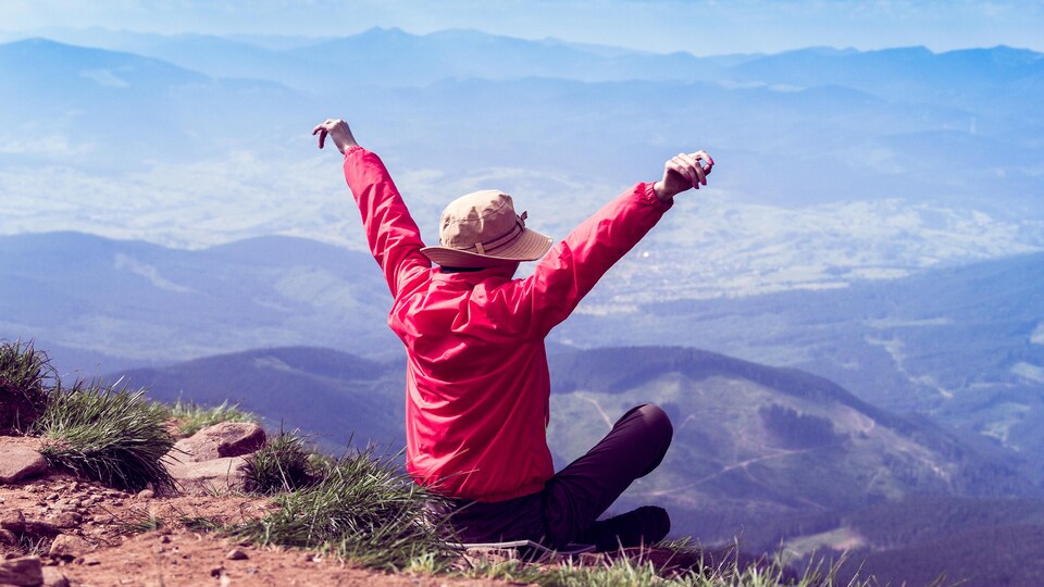 Une femme ouvre les bras devant un paysage montagneux.