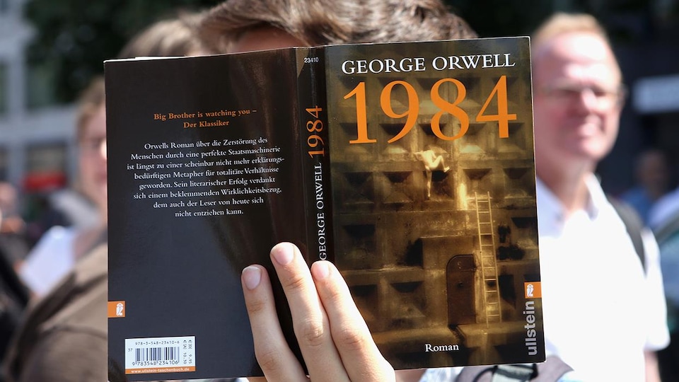 Une personne montre la couverture du roman 1984 de George Orwell.