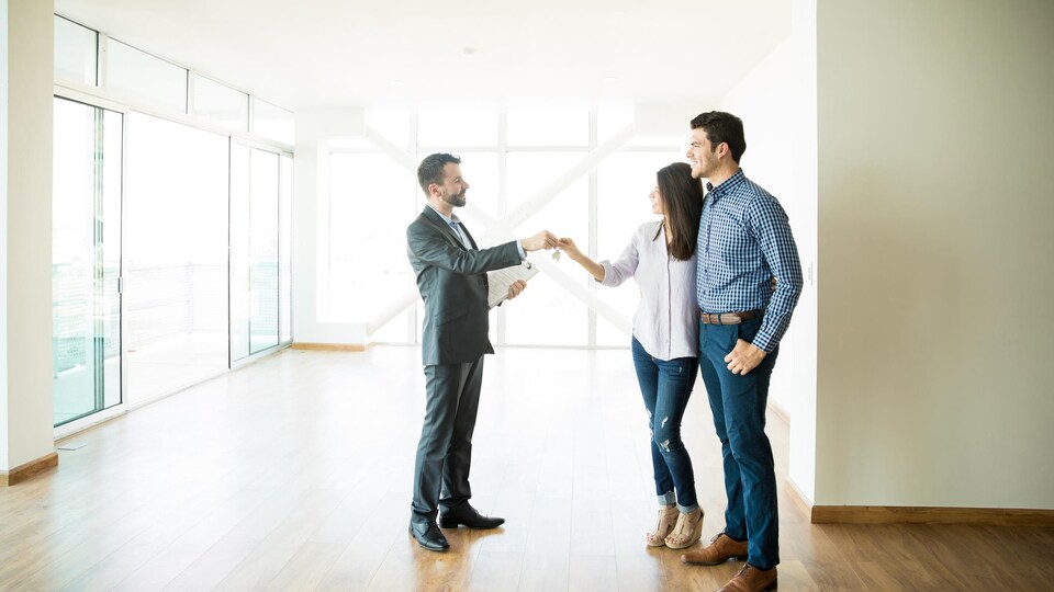 Un agent immobilier remet des clés à un couple d'acheteurs.