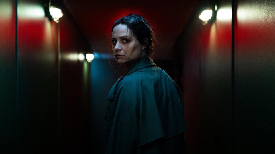 L'actrice jette un regard de dos, dans un couloir sombre.