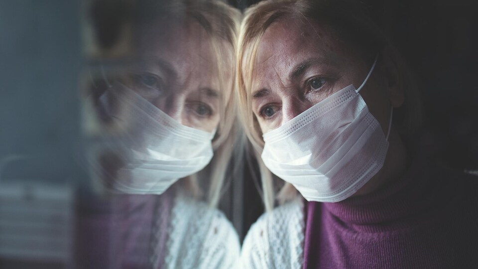 Une femme portant un masque a la tête appuyé sur une vitre.