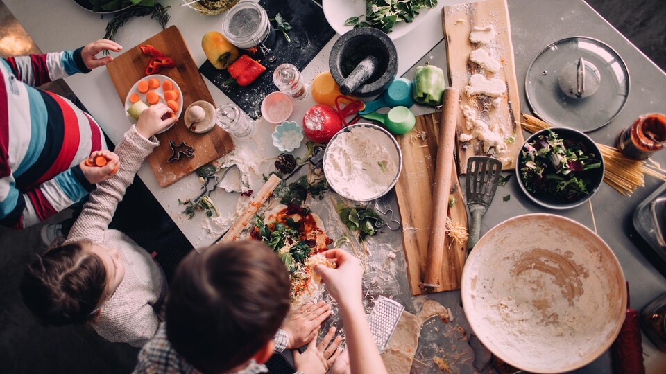 Deux enfants préparent à manger avec l'aide d'une femme.