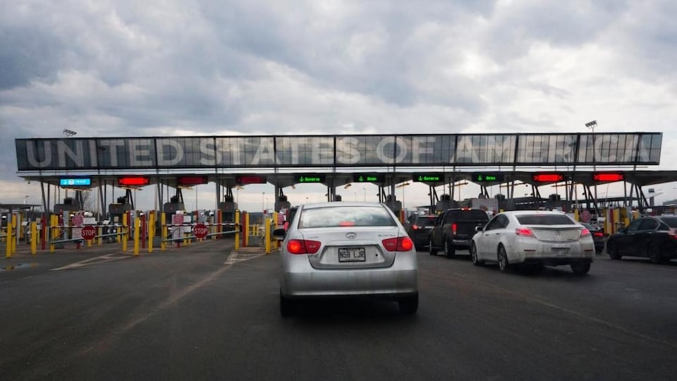 Des automobilistes en file avec l'inscription géante "United States of America" au-dessus des guérites du poste frontalier.