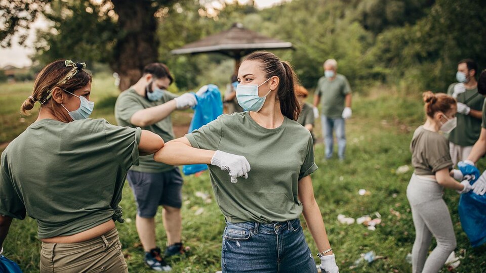 Une groupe d'hommes et de femmes portant des masques ramassent des déchets dans la nature.