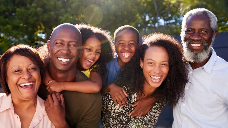 Une famille intergénérationnelle sourit à la caméra par temps ensoleillé.