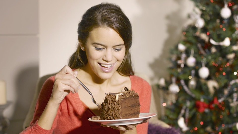 Une femme sourit et mange un gâteau au chocolat.