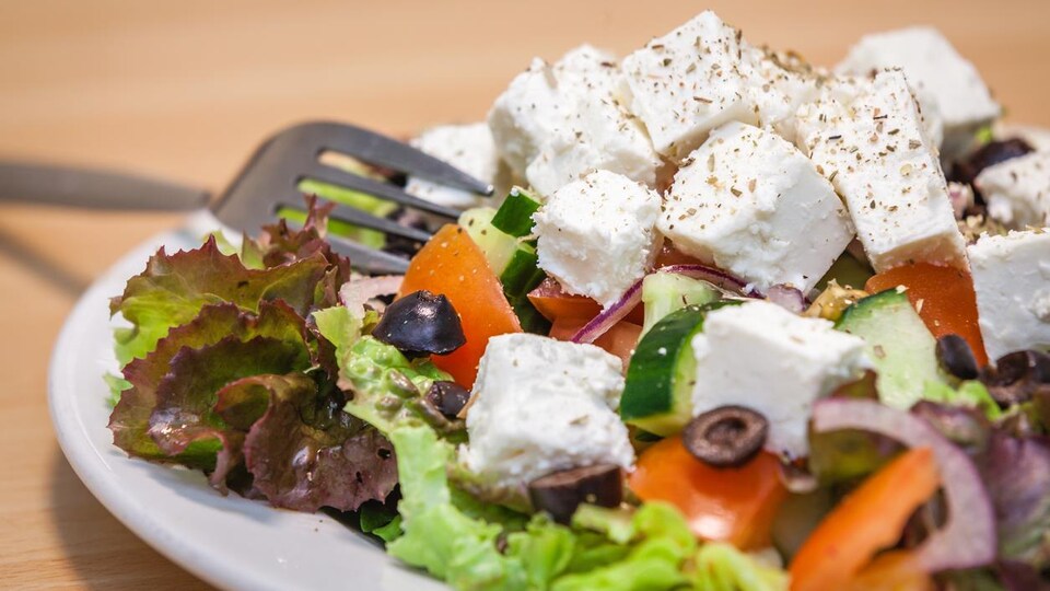 Une salade composée de feta, concombres, tomates, olives noires, oignons et laitue servie dans une assiette.