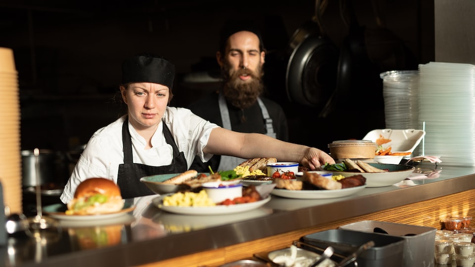 Deux cuisiniers disposent des plats sur un comptoir, dans un restaurant.