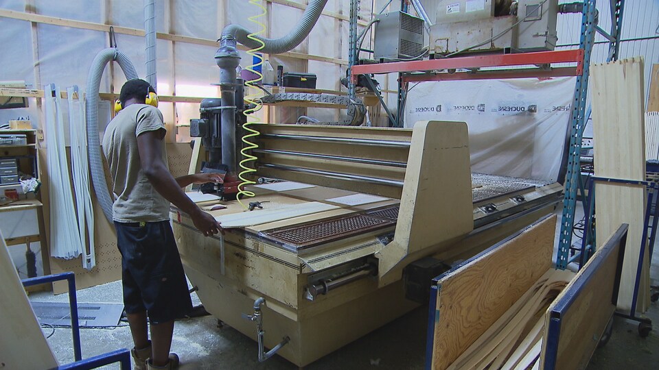Un ouvrier tient une planche de bois sur une machine industrielle.