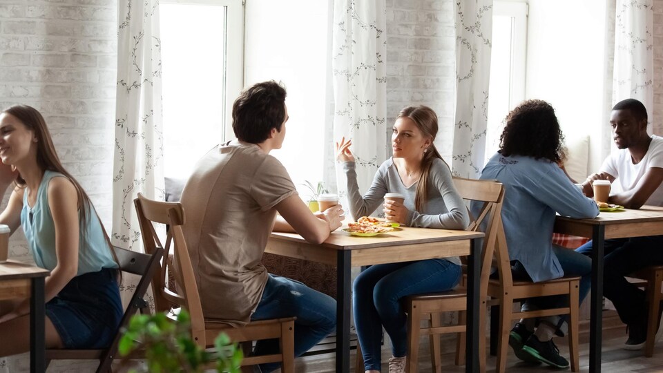 Des jeunes gens attablés à un restaurant discutent.